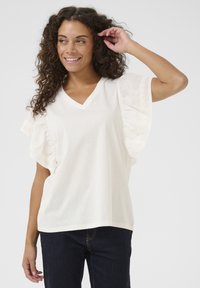 Top bianco a scollo a V con maniche arricciate e dettagli in pizzo, realizzato in tessuto leggero, abbinato a jeans in denim scuro.