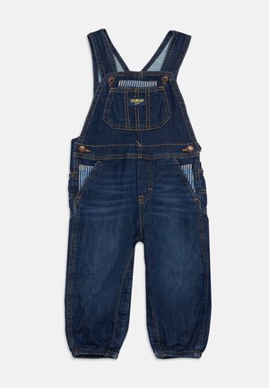 Salopette en denim bleu foncé pour tout-petit avec bretelles réglables, poche avant avec logo jaune, poches latérales avec doublure rayée et chevilles élastiquées.