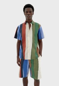 Ensemble en coton composé d'une chemise et d'un short à rayures multicolores ; présente de larges rayures verticales dans des teintes de bleu, vert, rouge et crème avec des boutons.