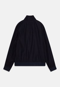Giacca leggera blu navy con colletto stand, polsini e orlo elasticizzati. Presenta un discreto dettaglio del logo sulla parte posteriore. Texture liscia.