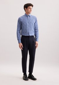 Camicetta azzurra chiara con motivo floreale, abbinata a pantaloni navy su misura e scarpe nere. Tessuto liscio, design del colletto standard.