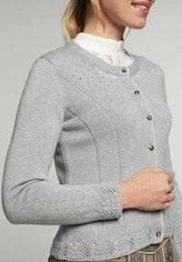 Cardigan en tricot gris avec un bouton à l'avant, détails décoratifs en œillets, texture côtelée et dentelle à l'ourlet et aux manches.