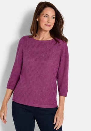 Maglione viola lavorato a maglia con scollo rotondo, maniche a tre quarti, motivo strutturato e orlo a coste. Indossato con pantaloni scuri.