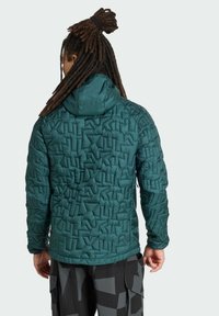 Groene gewatteerde jas met een textuurquiltontwerp en een capuchon; gemaakt van lichtgewicht materiaal. Zichtbare naden en een getailleerde pasvorm.