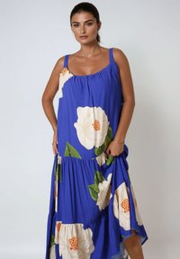 Blauwe bloemenmaxi-jurk met grote witte en oranje hibiscuspaterns, met een losse pasvorm, vierkante halslijn en brede schouderbanden.