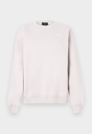 Jasnoróżowa bluza typu crewneck z długimi rękawami i małym białym logo Jumpman na lewej piersi.