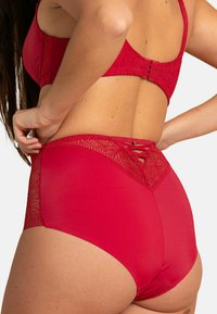Cet ensemble de lingerie rouge comprend un bas taille haute avec des détails en dentelle à l'arrière et un matériau lisse et ajusté pour le confort.