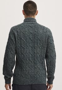 Dunkelgrüner Kabelstrickpullover mit hohem Kragen sowie gerippten Bündchen und Saum, aus strukturiertem, weichem Wollmaterial.