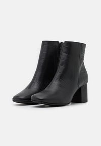 Botines negros hasta el tobillo con textura de piel de cocodrilo, puntera puntiaguda y tacón cuadrado. Cuenta con una cremallera lateral para facilitár su uso.