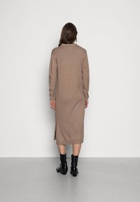 Robe en tricot marron à manches longues, avec une coupe droite, fentes latérales et ourlet côtelé. Portée avec des bottes noires à talons.