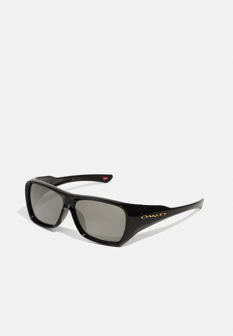 Óculos de sol de plástico preto com lentes cinzentas. Apresentam uma forma retangular e um logótipo dourado na armação. Acentos texturizados nas hastes.