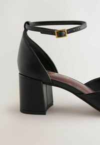 Sandale noire en cuir avec talon bloc, bride cheville et boucle dorée, dotée d'un talon carré et d'une conception à bout ouvert.