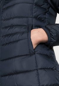 Giacca a vento blu navy con motivo trapuntato, dotata di tasca laterale e polsini elasticizzati. Tessuto morbido e materiale resistente all'acqua.