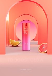 Siero Magico Pearly Power Shake di KIKO in una bottiglia rosa sfumata. Arcate circostanti in tonalità di rosa, con fette di arancia e pompelmo sul pavimento.
