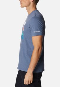 Camiseta de algodón azul de manga corta con un diseño gráfico colorido en la parte frontal y un logotipo en la manga izquierda.