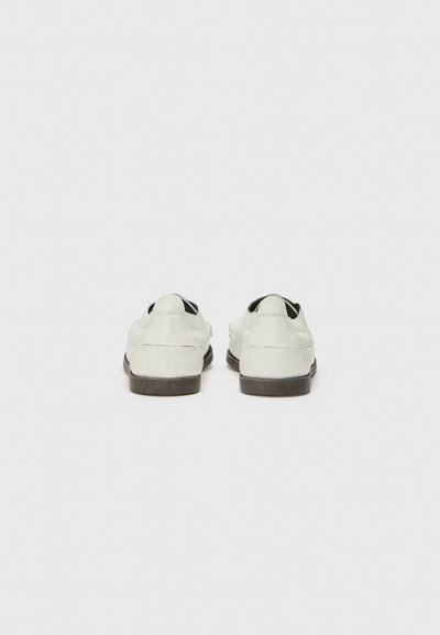 Scarpe in pelle bianca con punta arrotondata, tacco basso e finitura testurizzata. Presentano dettagli neri e un design minimalista sul retro.