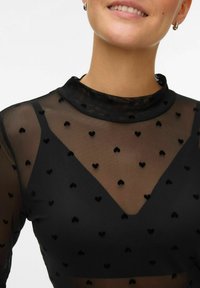 Zwart doorschijnend top met een hoge halslijn, voorzien van een hartpatroon. De mesh stof heeft een zachte textuur en een gelaagd ontwerp met een V-vormige uitsnijding.