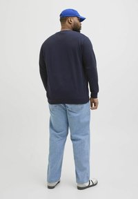 Navyblaues Sweatshirt mit langen Ärmeln, gerippten Bündchen und Saum, kombiniert mit hellblauen, lässigen Jeans und schwarzen Sandalen, von hinten betrachtet.