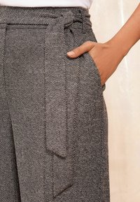 Šedé texturované kalhoty s herringbone vzorem, s vázacím pásem v pase a bočními kapsami, které předvádějí elegantní a dokonale střižený design.