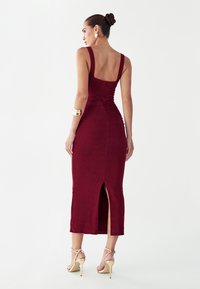 Vestido midi burdeos con una silueta ajustada, escote cuadrado, abertura lateral y tejido texturizado, con tirantes anchos y detalle fruncido en la parte trasera.