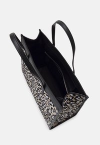 Taška s černými koženými držadly, jejíž vnější část je potažena látkou s leopardím potiskem. Uvnitř se nachází kapsa na zip a černá podšívka, s otevřeným vrchem.