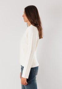 Maglione bianco a coste con silhouette aderente e maniche lunghe, abbinato a jeans in denim blu. Design semplice e tessuto texturizzato.