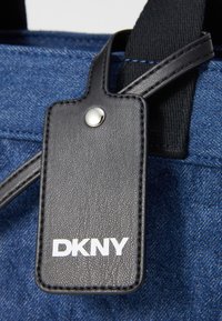 Zils audekla soma ar melnu teksturētu ādas birku, sudraba pogu un baltu "DKNY" logo. Melni auduma rokturi piestiprināti pie somas.