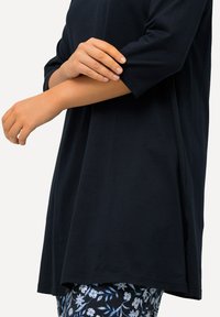 Tummansininen tunika, jossa on lyhyet hihat, pehmeää puuvillakangasta, rento malli ja sivurei'ät, yhdistettynä kuvioituihin kukkaleggingeihin.