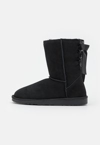 Sort ruskindstøvle med rund tå, ved læggen højde og snørebånd detaljer bagpå. Gummisål med en struktureret finish for godt greb.