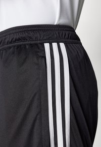 Sorte treningsshorts med hvit elastisk linning og tre vertikale hvite striper på siden, laget av et glatt og pustende materiale.