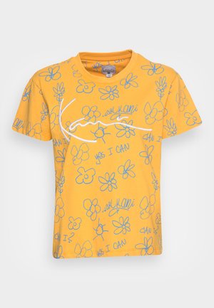 Gul bomulds-T-shirt med et legende design med blå blomsteromrids og tekst, inklusive "YES I CAN" og "kan I?" i forskellige placeringer.