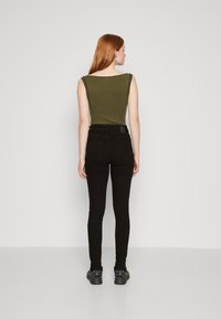 Ελαιώδους πράσινου ριγέ αμάνικο μπλουζάκι συνδυασμένο με μαύρα στενά τζιν. Το μπλουζάκι διαθέτει φαρδιές τιράντες, ενώ τα τζιν έχουν στενή εφαρμογή και μέση μεσαίου ύψους.