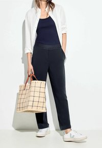 Granatowy top na ramiączkach, biała koszula na guziki, czarne spodnie na elastycznym pasie, beżowa torba w kratkę z brązowymi uchwytami i białe trampki.