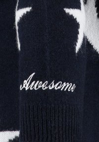 Maglione lavorato a maglia blu marino con motivi a stella bianchi e la parola "Awesome" ricamata in bianco sulla zona del gomito. Texture morbida e polsini a costine.
