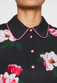 Camicia nera con stampa floreale; presenta bottoni rosa e rifinitura del colletto, texture simile alla seta, e un design di fiori rosa e bianchi.