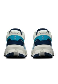 Baskets de course avec un dessus gris clair et bleu, un col rembourré et une semelle blanche épaisse. Présente un logo visible et des accents texturés.