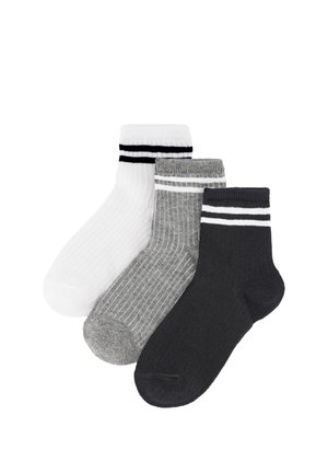 Tres calcetines tobilleros acanalados en blanco con rayas negras, gris con rayas blancas y negro con rayas blancas, colocados superpuestos sobre un fondo blanco.
