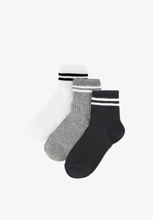 Tres calcetines tobilleros acanalados en blanco con rayas negras, gris con rayas blancas y negro con rayas blancas, colocados superpuestos sobre un fondo blanco.