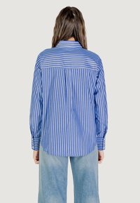 Camicia a maniche lunghe con bottoni, a righe blu e bianche, con yoke sul retro, vestibilità rilassata e orlo arrotondato, abbinata a jeans chiari.