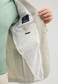Hellgrauer Blazer aus strukturiertem Stoff, mit cremefarbener Fütterung und geometrischem Muster sowie internen Etiketten mit der Aufschrift "JOOP!" und "SLIM FIT."