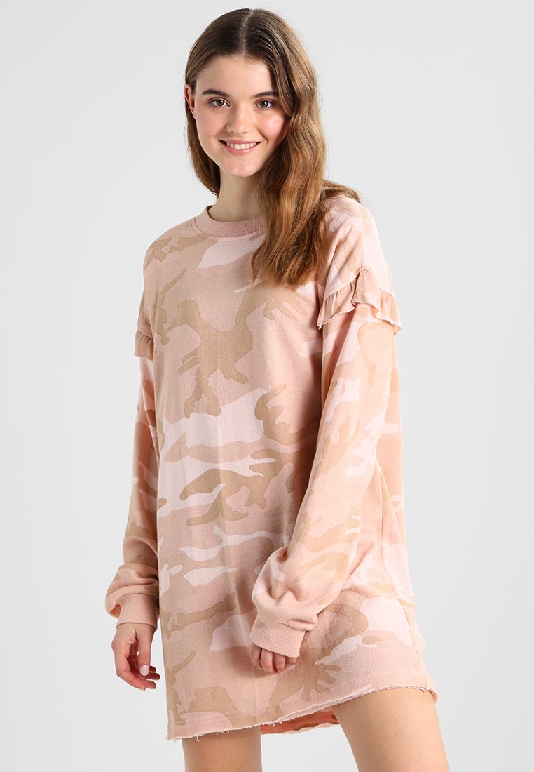 Lys rosa camo-mønstredd sweaterdress med lange ermer, volangdetaljer på skuldrene, myk tekstil og slitt kant.