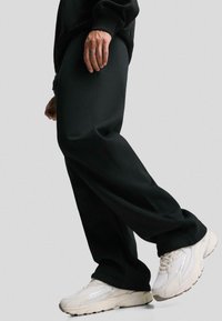 Black sweatpants with a loose fit, made of soft fabric, paired with beige sneakers featuring a textured upper and visible logo accents.