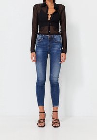 Sheer black long-sleeve button-up shirt, blue skinny jeans with distressed detailing, and black strappy heeled sandals.