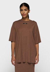Brun oversized t-shirt med rund halsudskæring og korte ærmer. Stoffet ser blødt og glat ud; har et lille sort logo ved kraven.