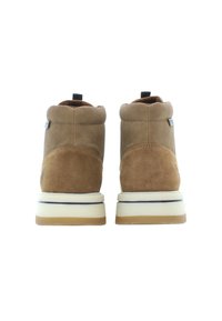 Stivali alla caviglia in suede marrone con una parte superiore in tessuto testurizzato, punta rotonda e suola in gomma bianca con un leggero accento beige.