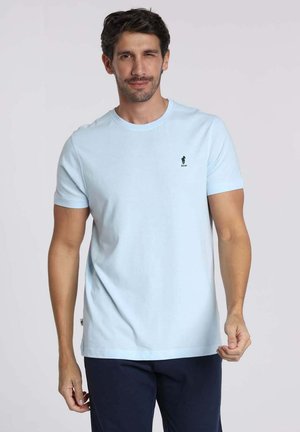 T-shirt en coton bleu clair avec un col rond et des manches courtes, présentant un petit logo noir sur la poitrine. Texture lisse.