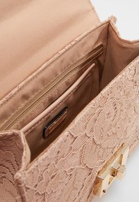Borsa a mano in pizzo rosa chiaro con un design floreale testurizzato, dotata di rivestimento in raso, tasca con zip e hardware in tono oro.