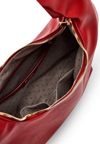 Red leather handbag with a zipped opening, featuring a gray interior with polka dot pattern, two zip compartments, and two open pockets.