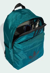 Zaino turchese con motivo esagonale, cerniera superiore e dettagli neri. All'interno si possono vedere occhiali da sole e una bottiglia d'acqua in acciaio inossidabile.