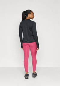 Sort langærmet top, lyserøde leggings med mønster og sorte træningssko. Refleksdetaljer på toppen, sporty pasform.